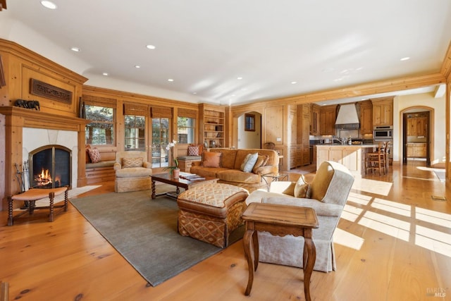 living room featuring arched walkways, a lit fireplace, recessed lighting, and light wood finished floors