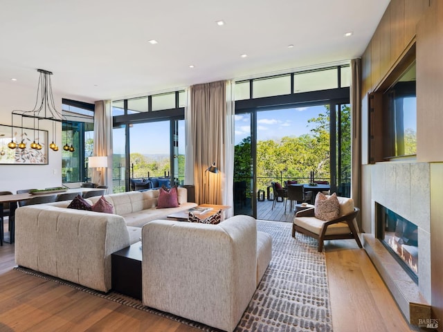living room with a glass covered fireplace, recessed lighting, wood finished floors, and a wall of windows