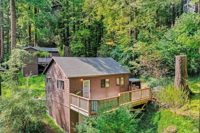 rear view of house featuring a forest view, a shingled roof, and a deck