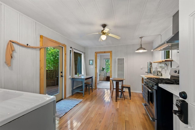 kitchen featuring light countertops, stainless steel range with gas cooktop, light wood-style floors, a ceiling fan, and wall chimney exhaust hood