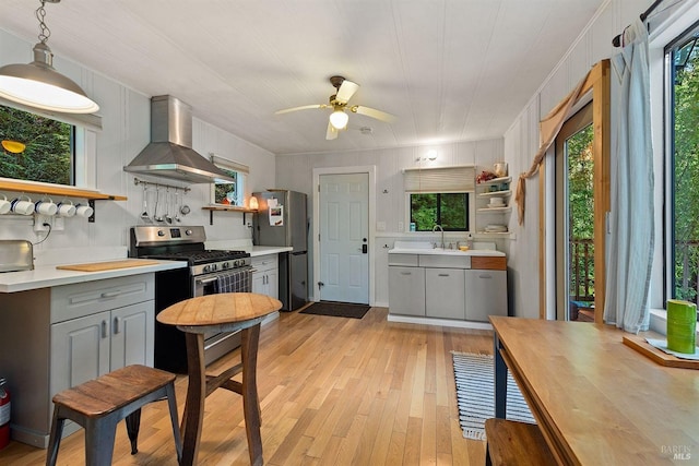 kitchen with open shelves, gray cabinets, stainless steel appliances, a sink, and wall chimney exhaust hood