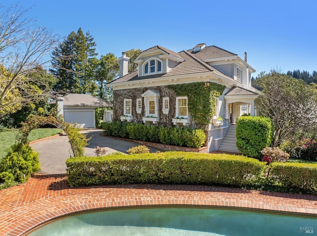 view of front of house featuring a garage, a chimney, a tile roof, an outdoor structure, and stucco siding