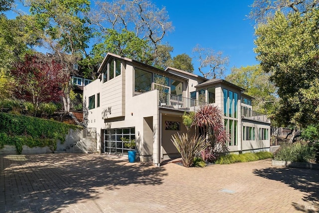 view of front of house with an attached garage, a balcony, stucco siding, stairway, and decorative driveway