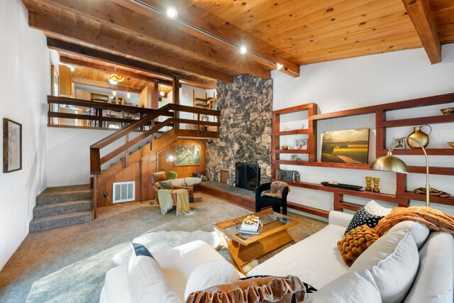 carpeted living room featuring beam ceiling, stairway, wood ceiling, a stone fireplace, and visible vents