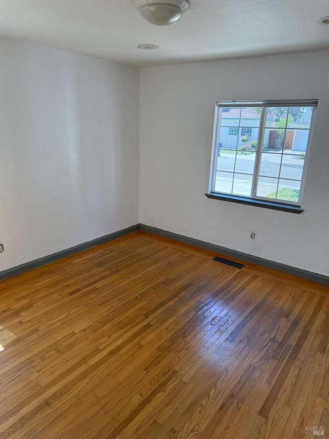 unfurnished room featuring baseboards, visible vents, and wood-type flooring