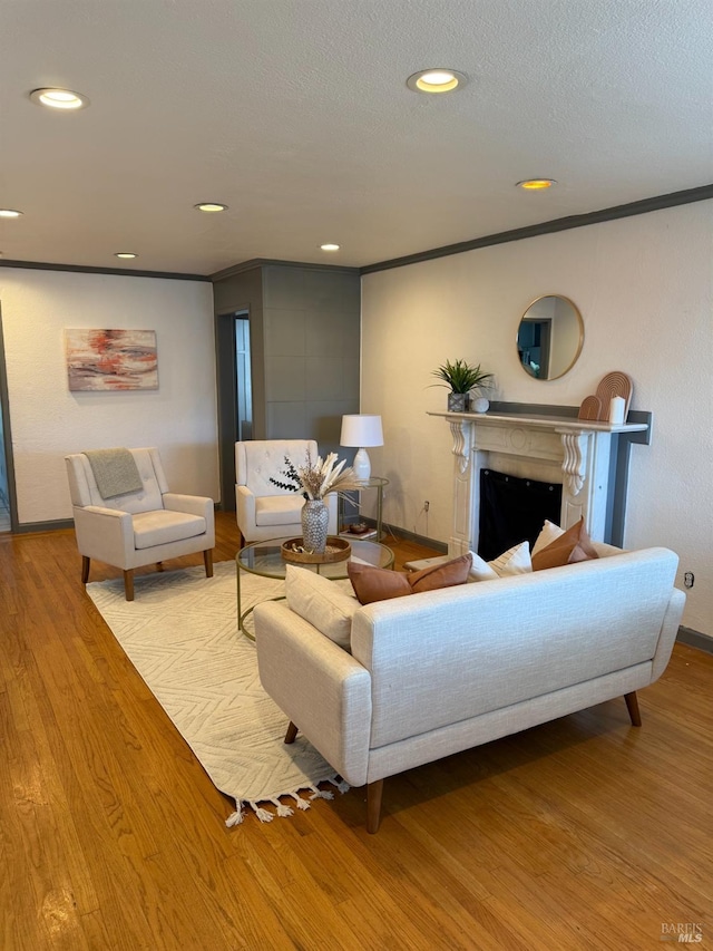 living area featuring a textured ceiling, a fireplace, wood finished floors, ornamental molding, and recessed lighting