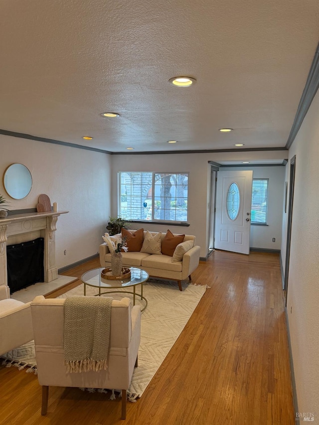 living room with crown molding, a fireplace, wood finished floors, a textured ceiling, and baseboards