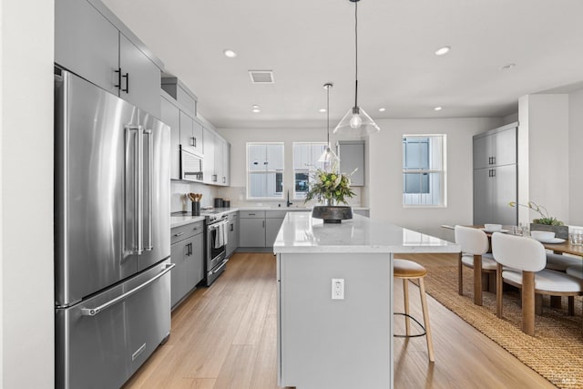 kitchen with appliances with stainless steel finishes, a kitchen bar, gray cabinets, a center island, and light wood-type flooring