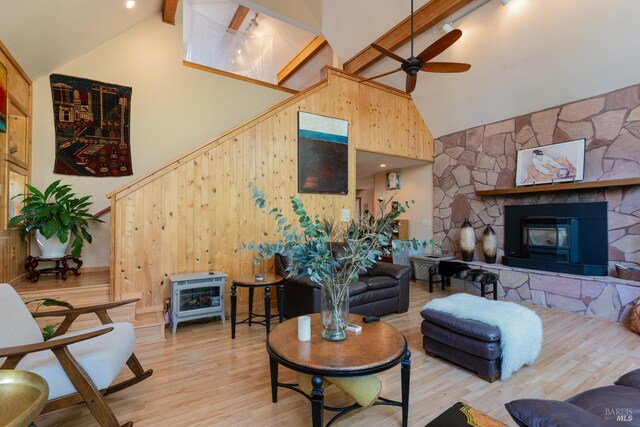 living room featuring a ceiling fan, wood finished floors, wood walls, a wood stove, and beamed ceiling