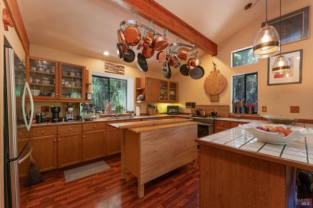 kitchen with freestanding refrigerator, tile counters, vaulted ceiling with beams, dark wood finished floors, and glass insert cabinets