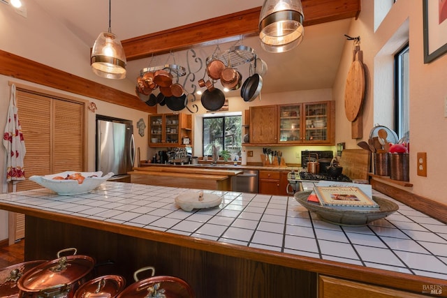 kitchen with brown cabinets, beam ceiling, appliances with stainless steel finishes, glass insert cabinets, and tile countertops