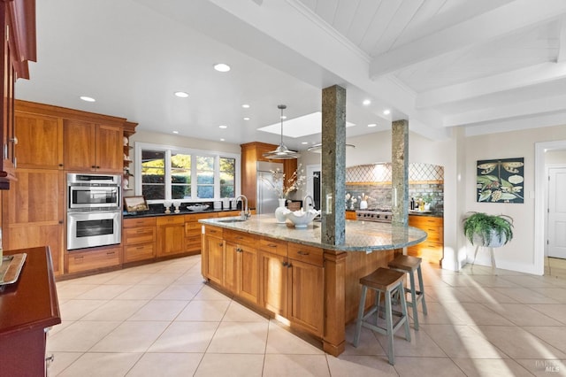 kitchen featuring stainless steel appliances, brown cabinetry, light tile patterned floors, and beam ceiling