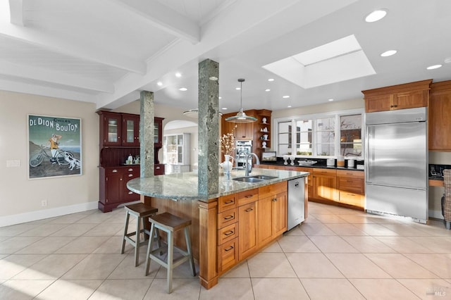 kitchen featuring a skylight, beam ceiling, appliances with stainless steel finishes, a sink, and light tile patterned floors