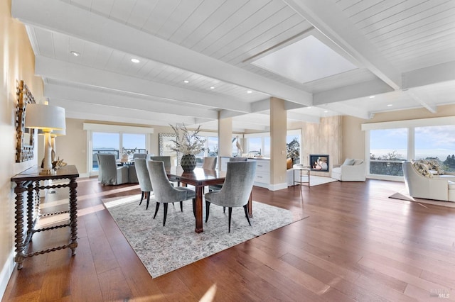 dining area featuring baseboards, beamed ceiling, a premium fireplace, and wood-type flooring