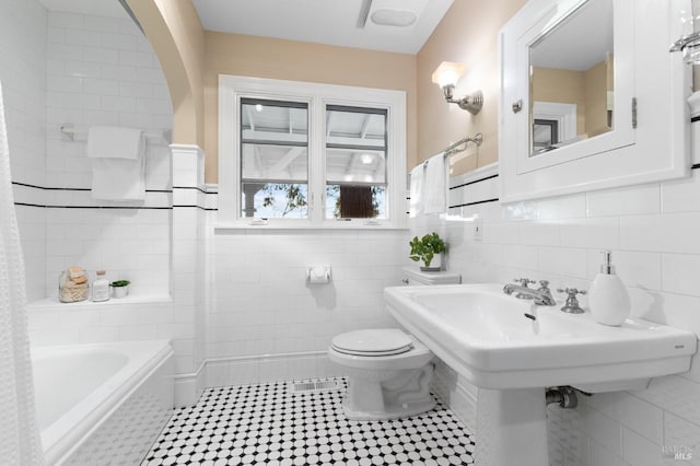 full bathroom featuring a bathing tub, toilet, tile walls, and tile patterned floors