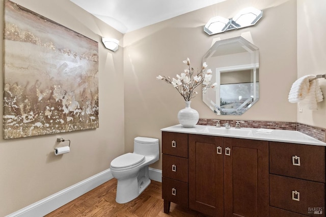 half bathroom with toilet, vanity, baseboards, and wood finished floors