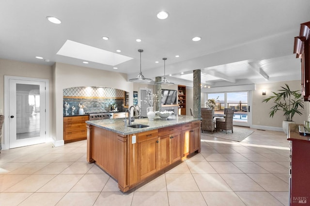 kitchen with decorative backsplash, a kitchen island with sink, a sink, and light tile patterned floors