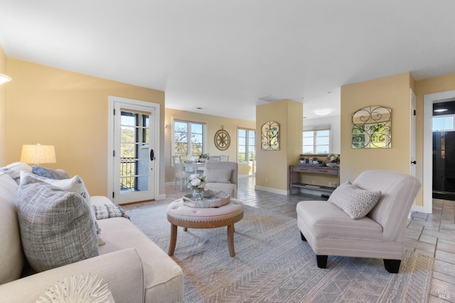 living area featuring baseboards, a healthy amount of sunlight, and stone tile flooring