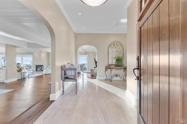entryway with ornamental molding, arched walkways, baseboards, and light wood finished floors