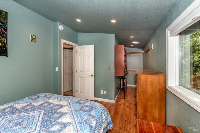 bedroom with baseboards, wood finished floors, recessed lighting, and a textured ceiling