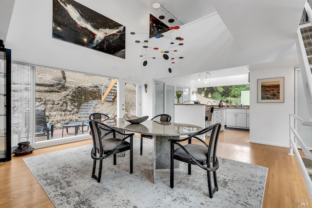 dining area with light wood-type flooring, a towering ceiling, and stairs