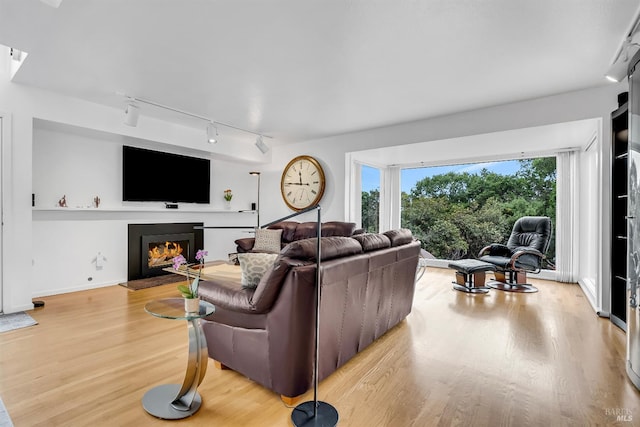 living room featuring track lighting, wood finished floors, baseboards, and a warm lit fireplace