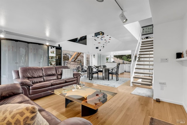 living area featuring lofted ceiling, track lighting, light wood-style floors, baseboards, and stairs