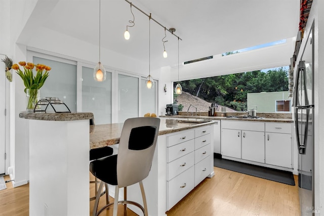 kitchen with a kitchen breakfast bar, light stone counters, light wood-type flooring, pendant lighting, and white cabinetry