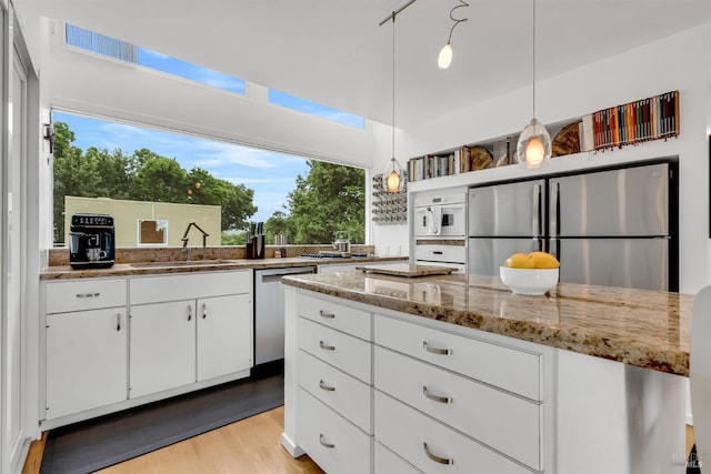 kitchen featuring a sink, light wood-type flooring, white cabinets, appliances with stainless steel finishes, and light stone countertops