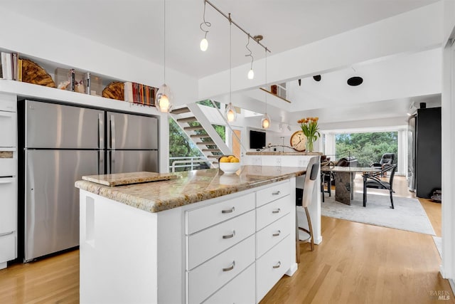 kitchen with freestanding refrigerator, light wood-style floors, light stone countertops, hanging light fixtures, and white cabinetry