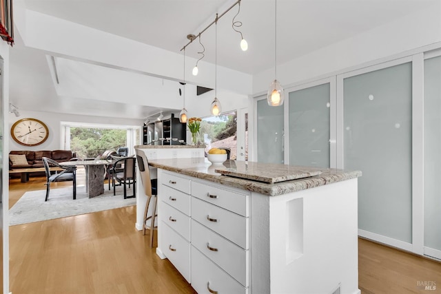 kitchen with a center island, pendant lighting, light wood-style flooring, white cabinetry, and light stone countertops
