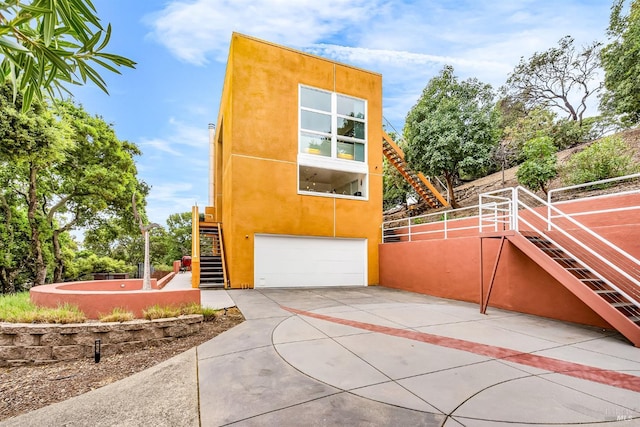 view of property exterior with stucco siding, an attached garage, concrete driveway, and stairs