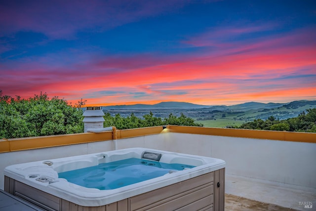 pool at dusk with a covered hot tub and a mountain view