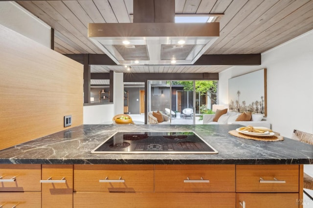 kitchen with dark stone counters, beam ceiling, island range hood, black electric stovetop, and open floor plan