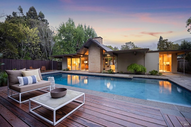 pool at dusk featuring a fenced in pool, an outdoor hangout area, a deck, and fence