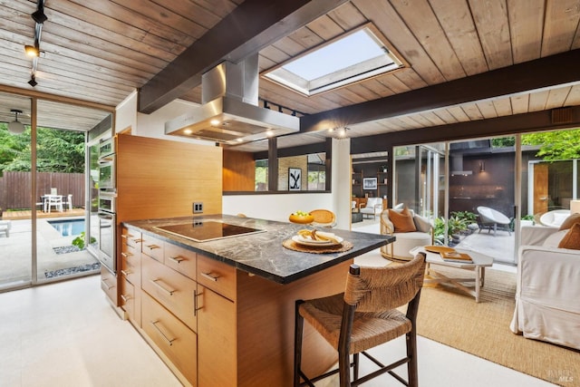 kitchen with island range hood, a skylight, black electric cooktop, plenty of natural light, and beamed ceiling