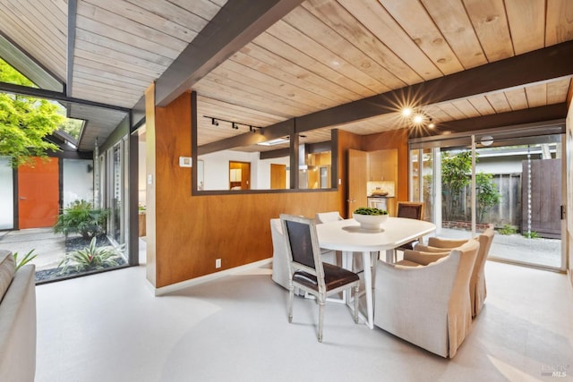 dining space featuring baseboards, beam ceiling, wood walls, and wooden ceiling