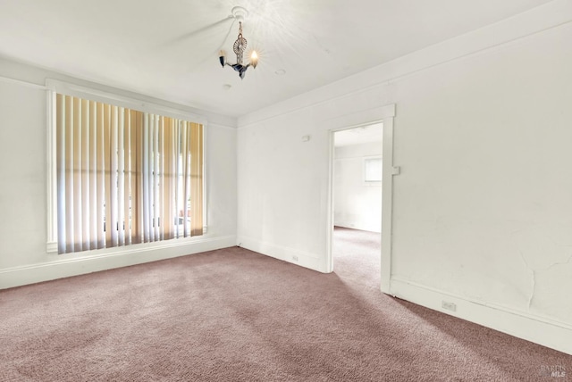 carpeted empty room featuring an inviting chandelier and baseboards