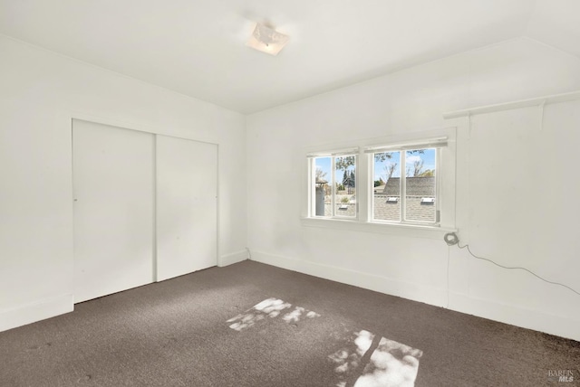 unfurnished bedroom featuring a closet, baseboards, dark colored carpet, and vaulted ceiling