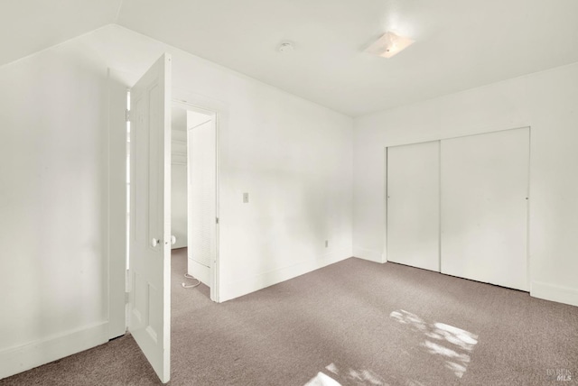 unfurnished bedroom featuring lofted ceiling, a closet, and carpet