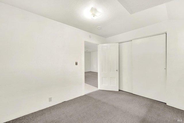 unfurnished bedroom featuring vaulted ceiling, a closet, and carpet floors