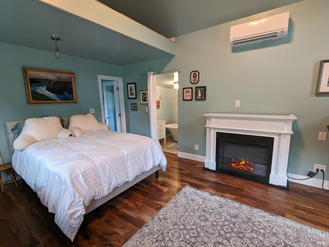 11900 Hwy 116, Guerneville, CA 95446 - bedroom featuring connected bathroom, a glass covered fireplace, baseboards, a wall unit AC, and wood finished floors