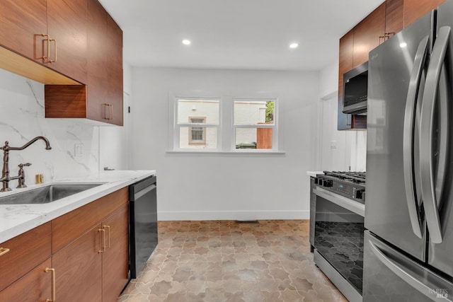 kitchen with decorative backsplash, baseboards, appliances with stainless steel finishes, a sink, and light stone counters