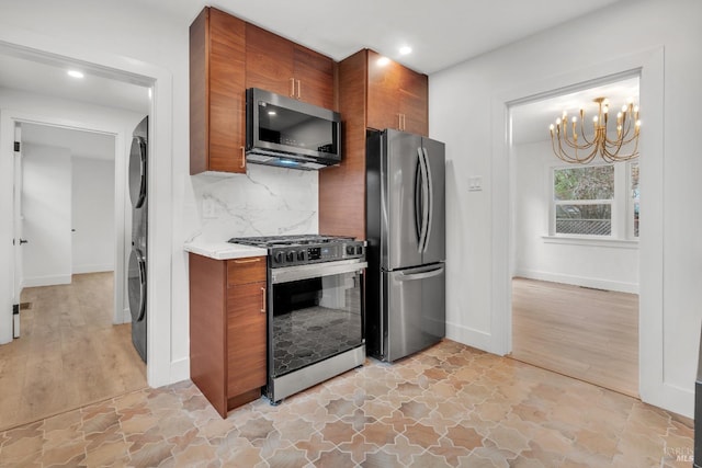 kitchen with tasteful backsplash, appliances with stainless steel finishes, a notable chandelier, stone finish flooring, and brown cabinetry