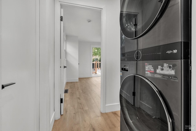 laundry area with light wood-style flooring, stacked washer and clothes dryer, baseboards, and laundry area