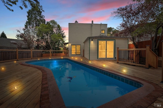 pool at dusk with a wooden deck, fence, and a fenced in pool