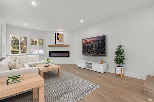 living room featuring baseboards, recessed lighting, light wood-style floors, and a glass covered fireplace