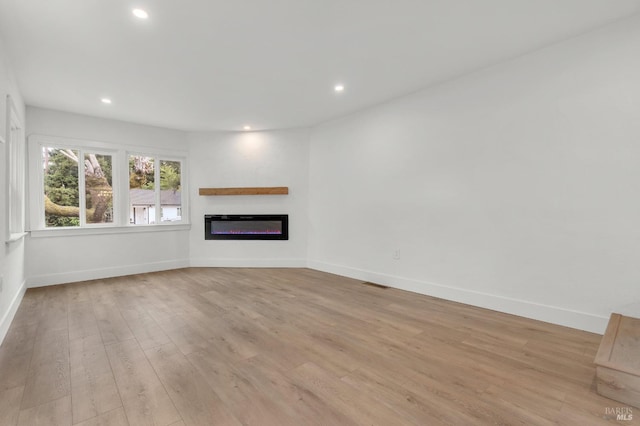 unfurnished living room with recessed lighting, baseboards, light wood-style floors, visible vents, and a glass covered fireplace