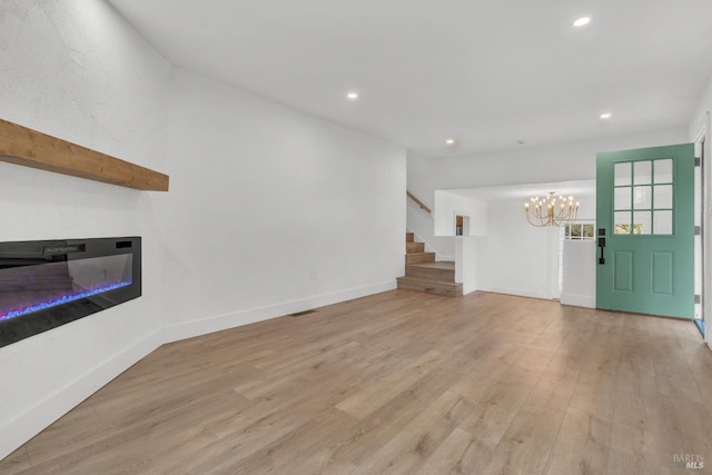 unfurnished living room featuring a notable chandelier, recessed lighting, stairway, and light wood-type flooring