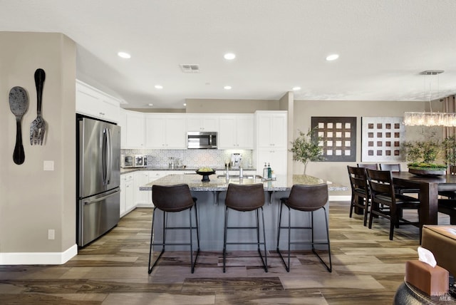 kitchen with wood finished floors, white cabinets, baseboards, appliances with stainless steel finishes, and visible vents